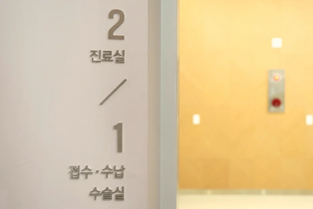 65세 이상 임플란트 건강보험 — 2층 진료실과 1층 접수·수납·수술실을 안내하는 층별 표지 (더이로운치과의원)