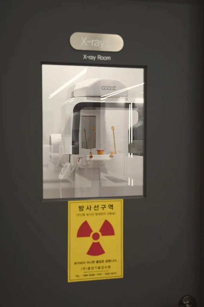 임플란트 뼈이식 — 방사선 안전 표시가 붙은 치과 촬영실 출입문 (더이로운치과의원)